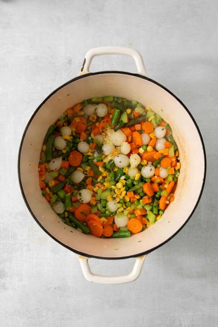 This homemade Chicken Pot Pie Soup recipe features a creamy broth that’s loaded with chicken and vegetables and topped with biscuits. The vegetables are added to the broth in a pot.