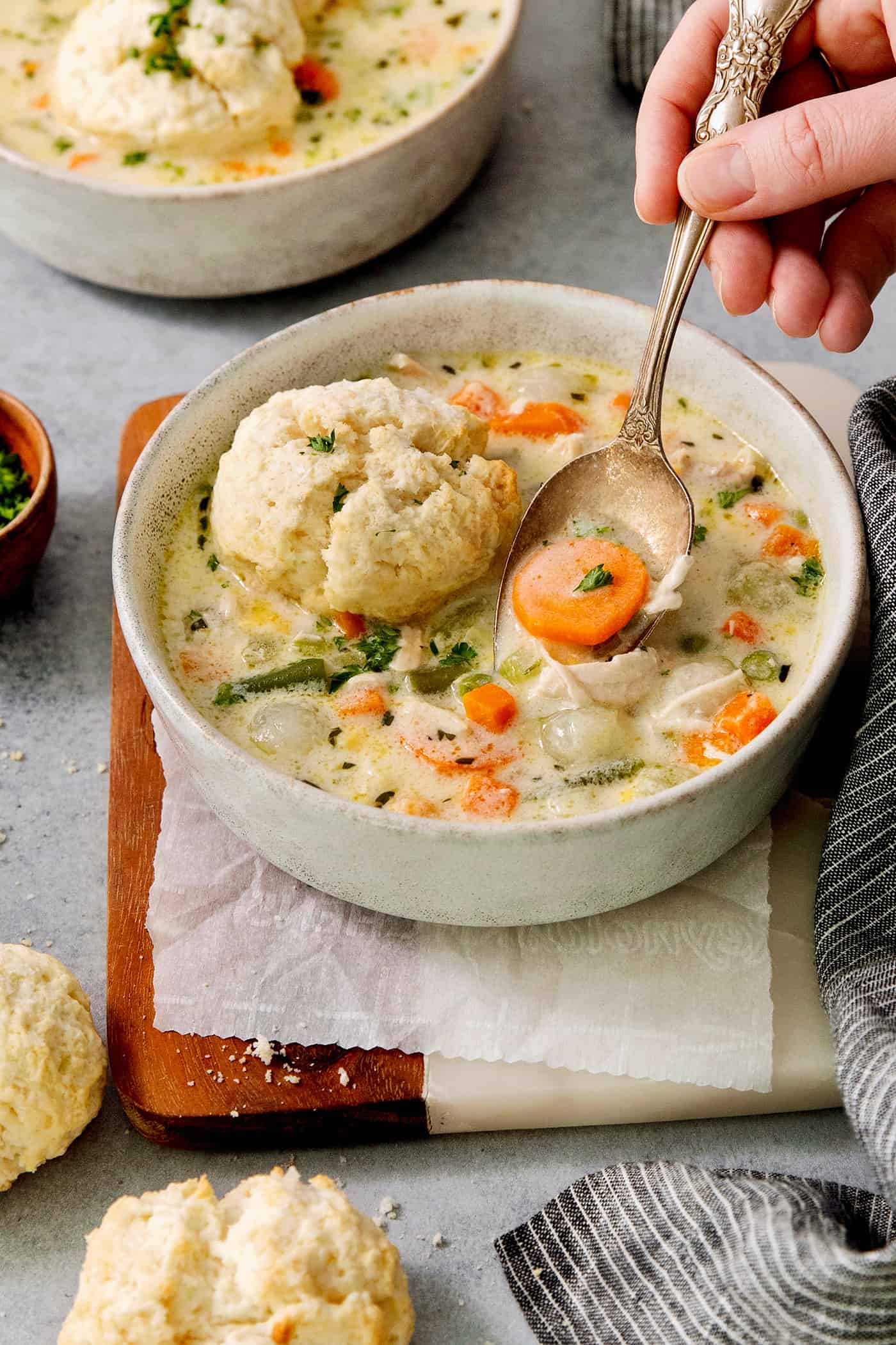 This homemade Chicken Pot Pie Soup recipe features a creamy broth that’s loaded with chicken and vegetables and topped with biscuits. A hand holding a spoon lifts out a spoonful of chicken pot pie soup.