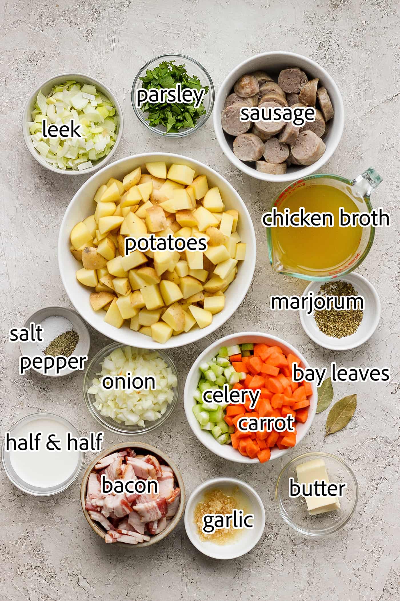 This German Potato Soup recipe is packed with savory sausage, salty bacon, and plenty of vegetables plus a spoonful of half-and-half. Ingredients needed to make German potato soup are shown: sausage, bacon, half and half, carrots, leek, onion, celery, chicken broth, bay leaf, parlsey.