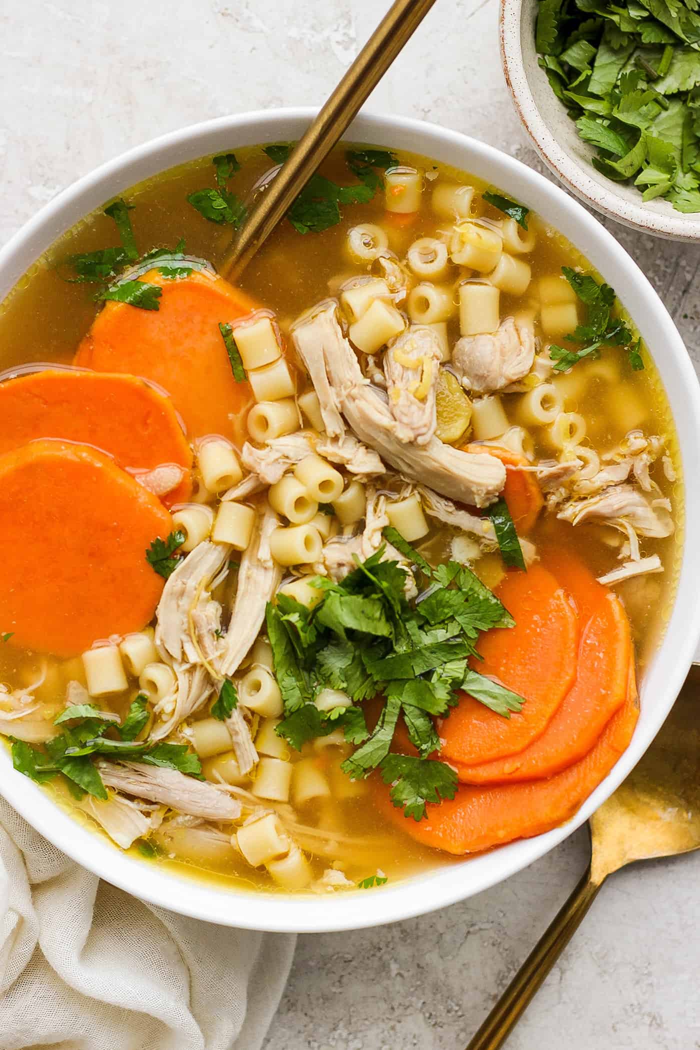 This zesty Chicken Ginger Soup recipe is brimming with fresh ginger, garlic, and lemon plus sweet potatoes, shredded chicken, and pasta. A hearty bowl of ginger chicken soup showing shredded chicken, sliced sweet potatoes, and pasta.