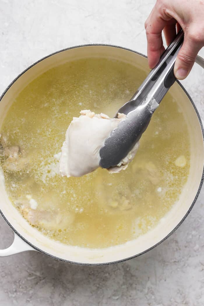 This zesty Chicken Ginger Soup recipe is brimming with fresh ginger, garlic, and lemon plus sweet potatoes, shredded chicken, and pasta. Tongs are used to remove the chicken from the broth.