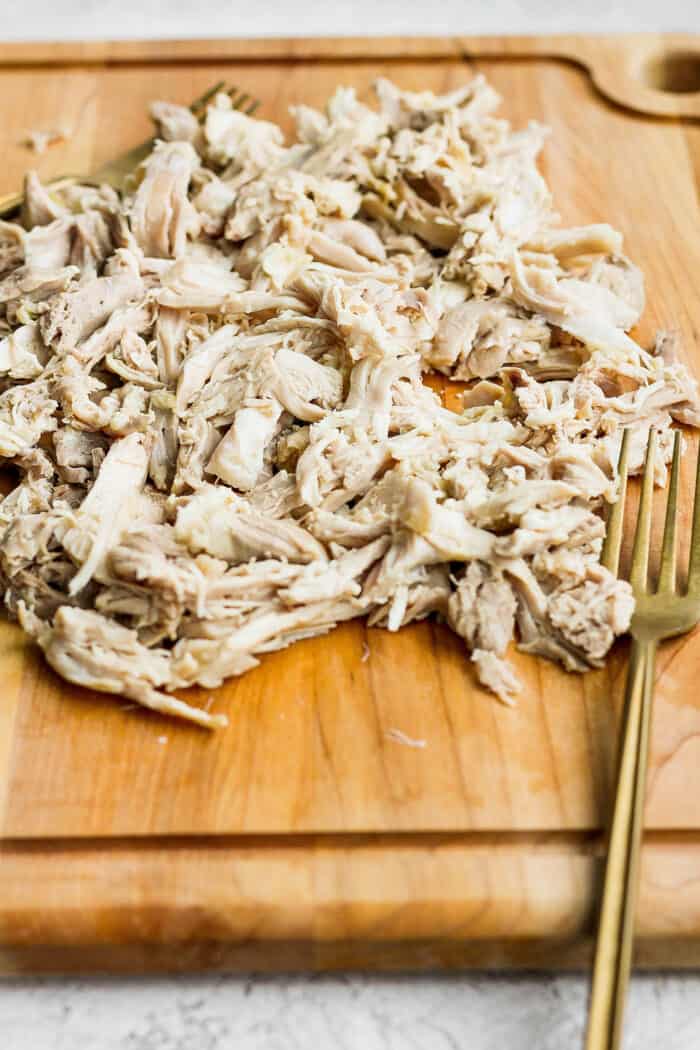 This zesty Chicken Ginger Soup recipe is brimming with fresh ginger, garlic, and lemon plus sweet potatoes, shredded chicken, and pasta. Shredded chicken on a wooden cutting board.