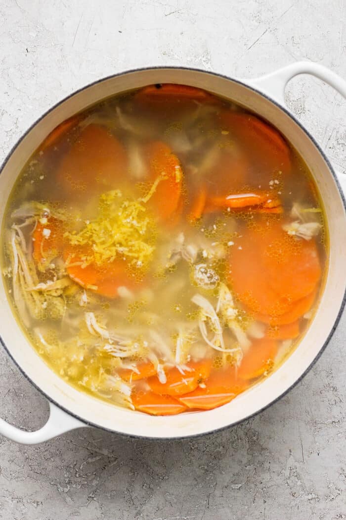 This zesty Chicken Ginger Soup recipe is brimming with fresh ginger, garlic, and lemon plus sweet potatoes, shredded chicken, and pasta. Sweet potato slices float on the top of a pot of ginger chicken soup.