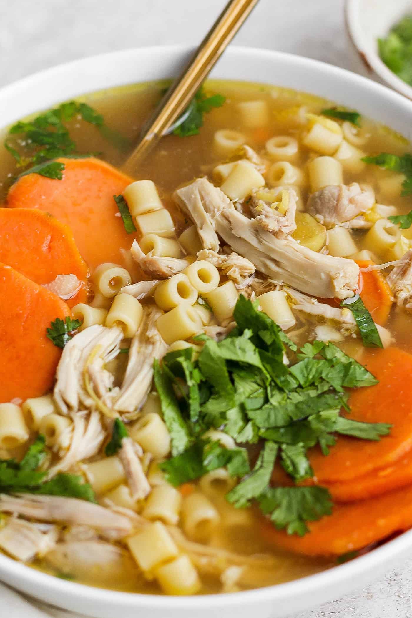 This zesty Chicken Ginger Soup recipe is brimming with fresh ginger, garlic, and lemon plus sweet potatoes, shredded chicken, and pasta. A bowl of ginger chicken soup topped with shredded chicken and sweet potatoes.
