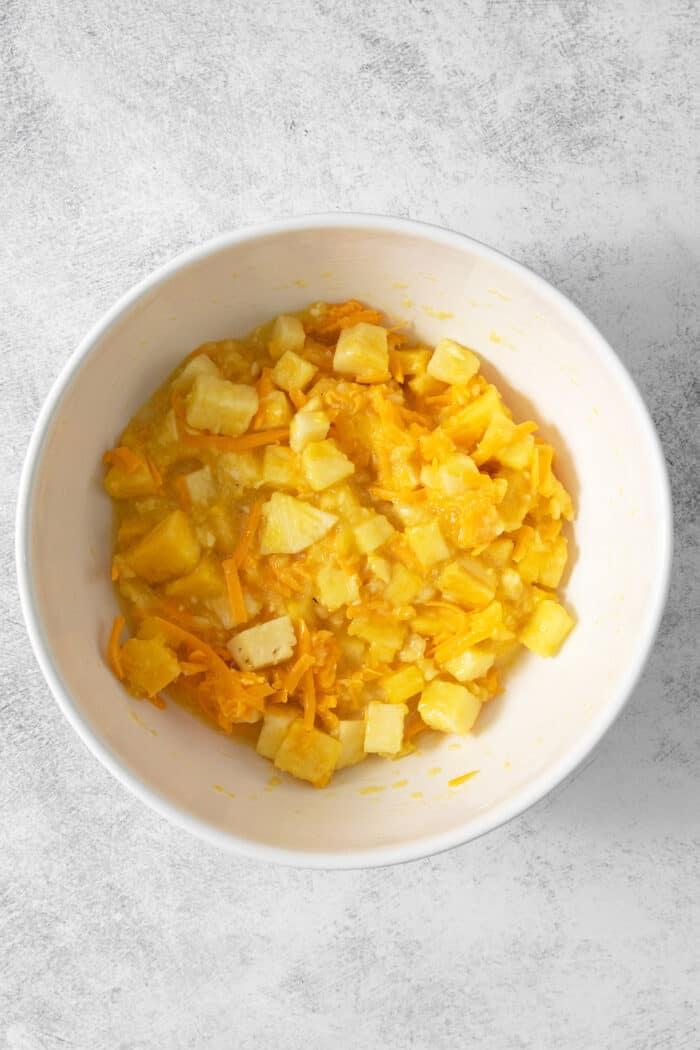 This easy Pineapple Casserole is a sweet and savory southern-inspired dish combining pineapple with cheese that pairs perfectly with BBQ. Whole pineapple chunks and shredded cheddar cheese are added to the pineapple puree in a bowl.