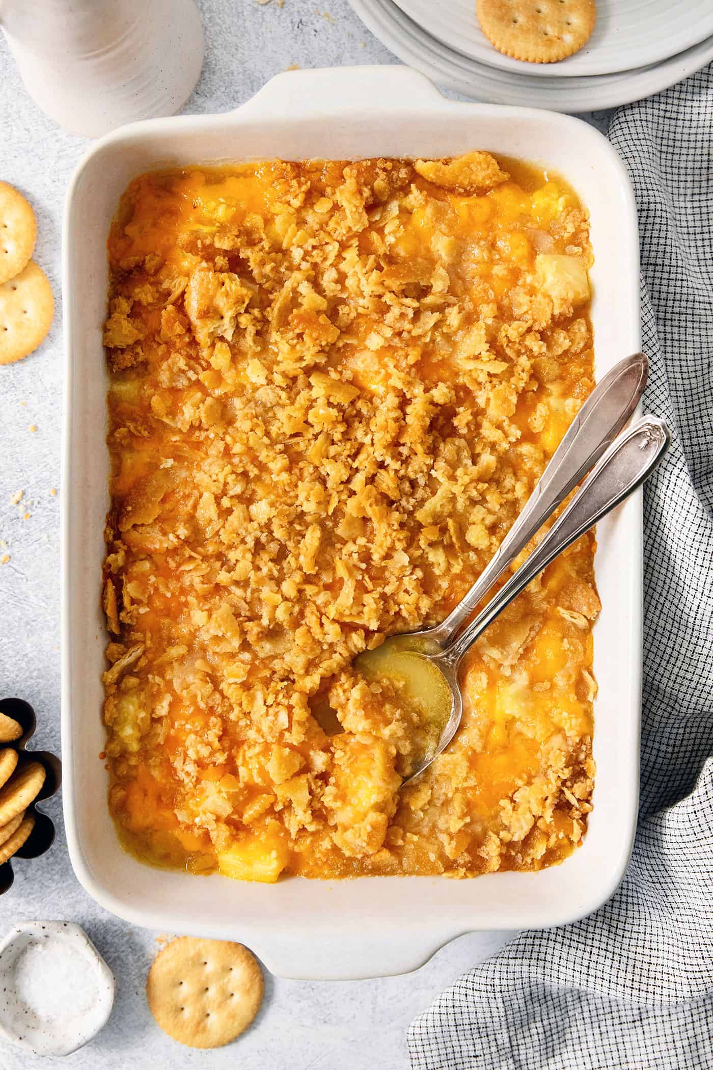 This easy Pineapple Casserole is a sweet and savory southern-inspired dish combining pineapple with cheese that pairs perfectly with BBQ. A serving spoon digs into a white baking dish holding pineapple casserole.