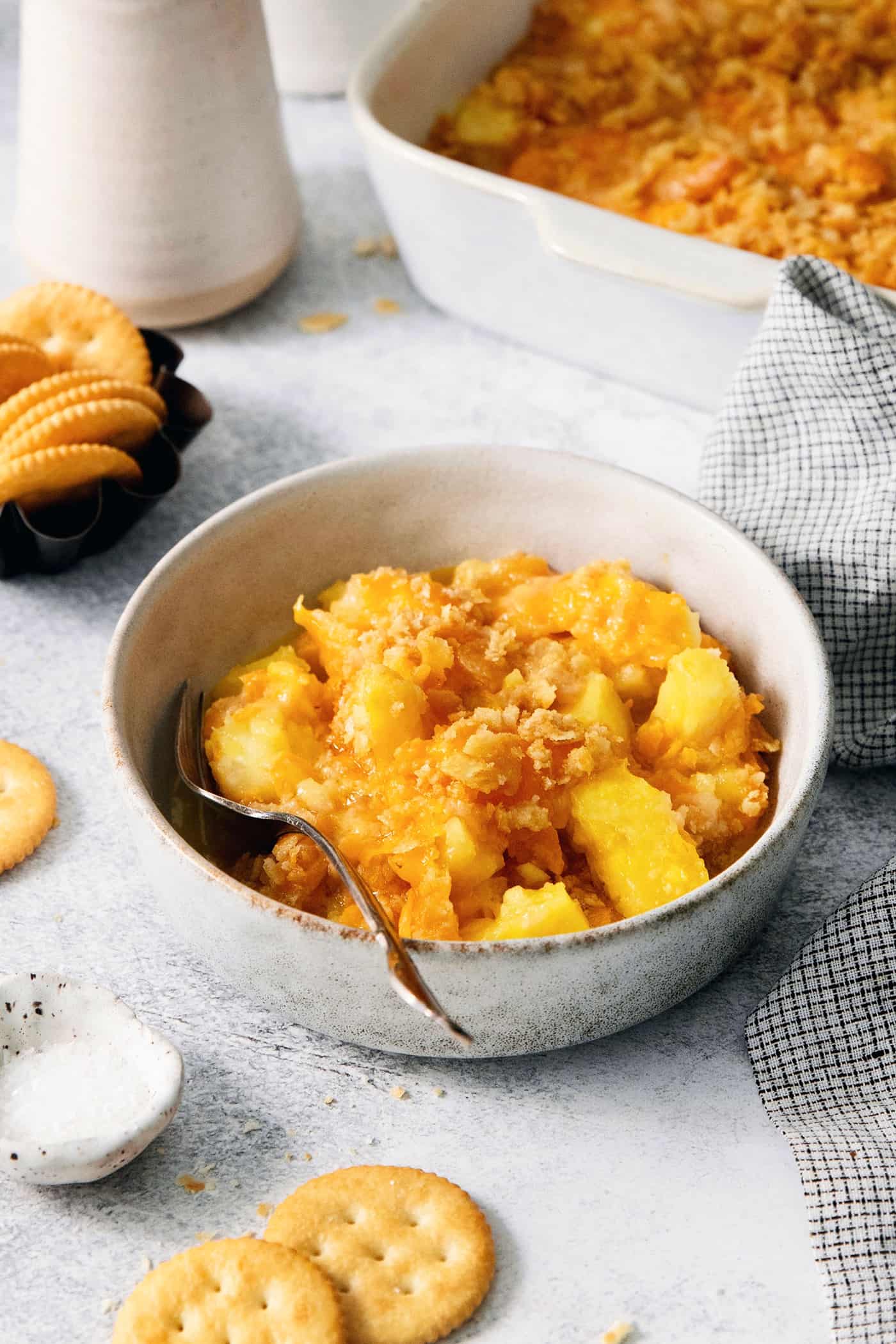 This easy Pineapple Casserole is a sweet and savory southern-inspired dish combining pineapple with cheese that pairs perfectly with BBQ. A white bowl holds a serving of pineapple casserole with a spoon.