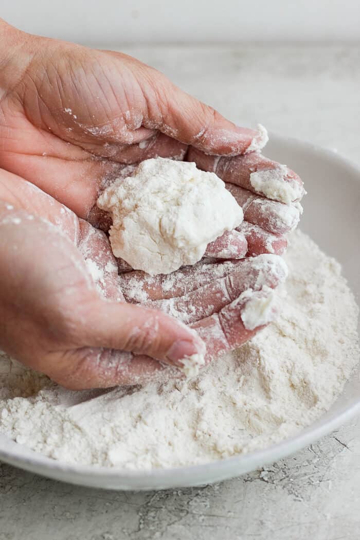 Flaky and light Touch of Grace Biscuits are made with White Lily flour to make unbelievably tender pull-apart biscuits. Two cupped hands hold a piece of biscuit over a bowl of flour.