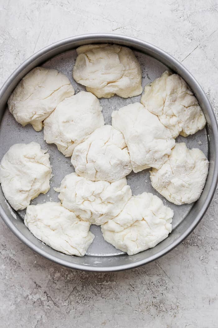 Flaky and light Touch of Grace Biscuits are made with White Lily flour to make unbelievably tender pull-apart biscuits. Touch of grace biscuit dough pieces are arranged in a metal baking round.