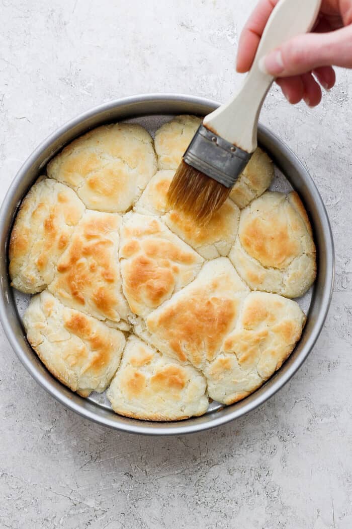 Flaky and light Touch of Grace Biscuits are made with White Lily flour to make unbelievably tender pull-apart biscuits. A hand uses a pastry brush to brush the baked biscuits with melted butter.