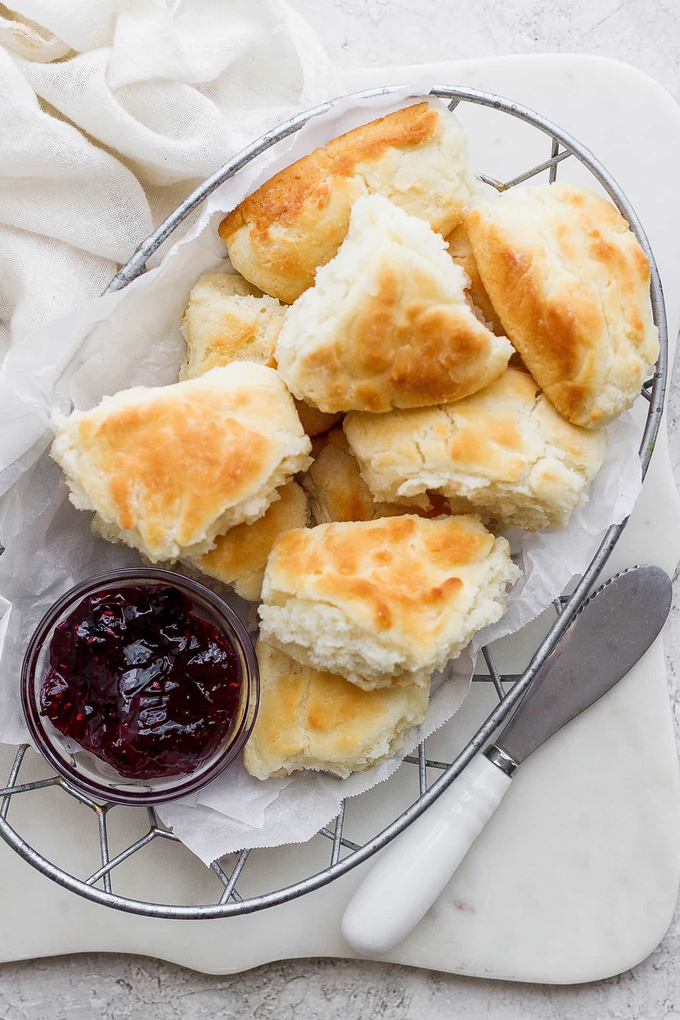 Flaky and light Touch of Grace Biscuits are made with White Lily flour to make unbelievably tender pull-apart biscuits. A wire basket holds browned touch of grace biscuits with a bowl of jam.