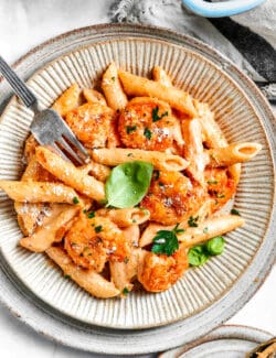 A fork picks up a piece of shrimp from a plate of cajun shrimp pasta.