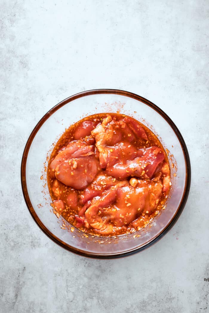 The pieces of chicken marinate in a glass bowl.