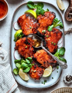 A platter of lemongrass chicken with lime wedges and basil.