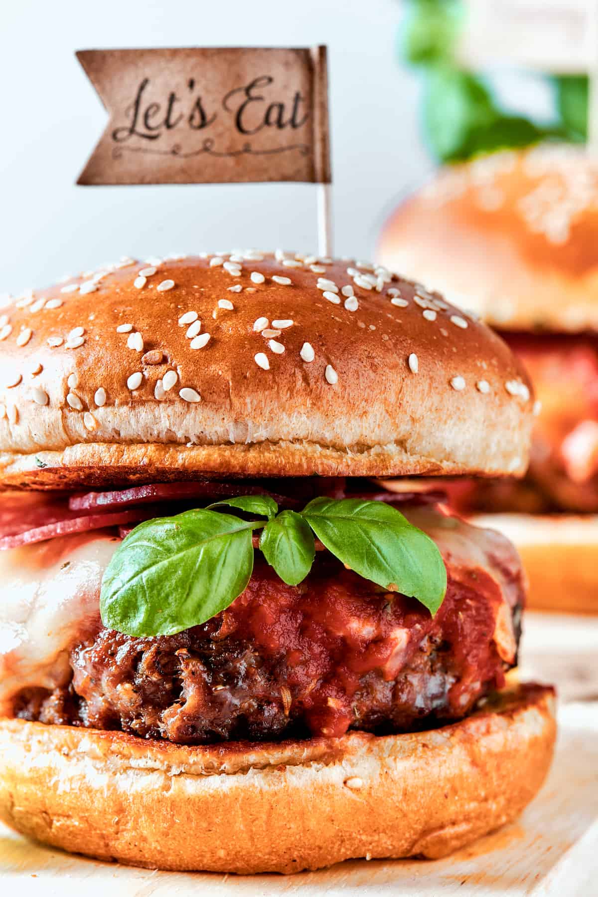 Blend two favorites to make this Pizza Burger recipe! Juicy beef patties are topped with tangy marinara, pepperoni, mozzarella & fresh basil. A close up of a beef patty made into a pizza burger.