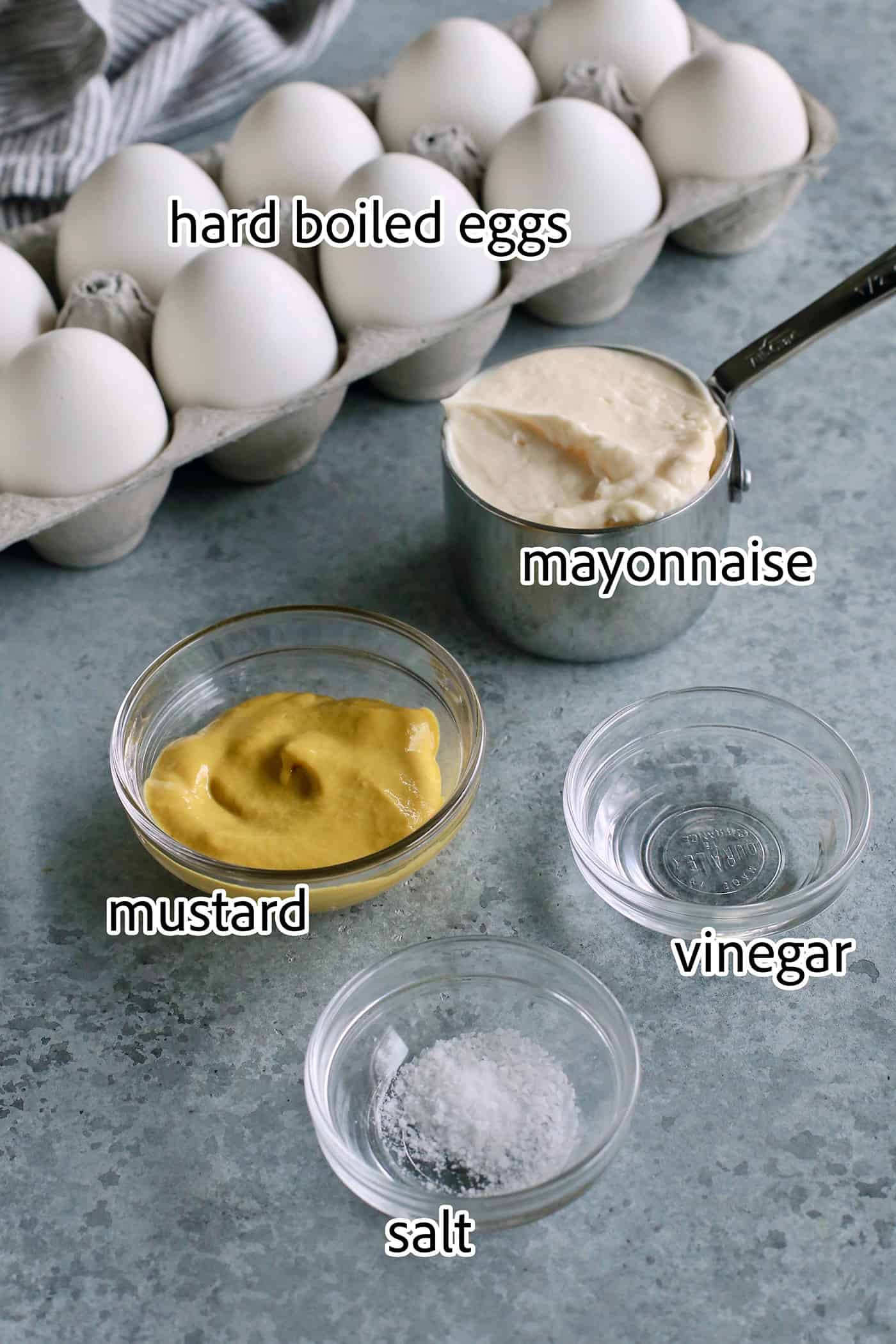 This Classic Deviled Eggs recipe is a beloved appetizer that features an irresistibly creamy and tangy filling made with simple basics. Make this easy deviled eggs recipe as written or try some of my flavorful variation suggestions. Ingredients for classic deviled eggs are shown: hard boiled eggs, mustard, mayonnaise, vinegar, salt.