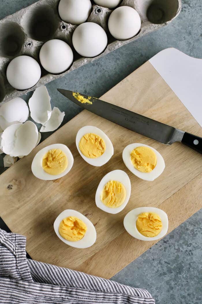 This Classic Deviled Eggs recipe is a beloved appetizer that features an irresistibly creamy and tangy filling made with simple basics. Make this easy deviled eggs recipe as written or try some of my flavorful variation suggestions. Peeled hard boiled eggs are cut in half on a cutting board.