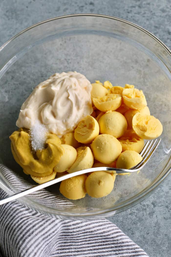 This Classic Deviled Eggs recipe is a beloved appetizer that features an irresistibly creamy and tangy filling made with simple basics. Make this easy deviled eggs recipe as written or try some of my flavorful variation suggestions. The hard boiled egg yolks are combined with mayonnaise, mustard, salt, and vinegar in a glass bowl.