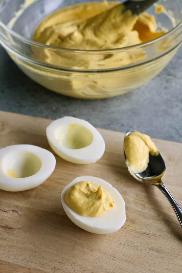 This Classic Deviled Eggs recipe is a beloved appetizer that features an irresistibly creamy and tangy filling made with simple basics. Make this easy deviled eggs recipe as written or try some of my flavorful variation suggestions. Adding the filling to the egg whites with a spoon.