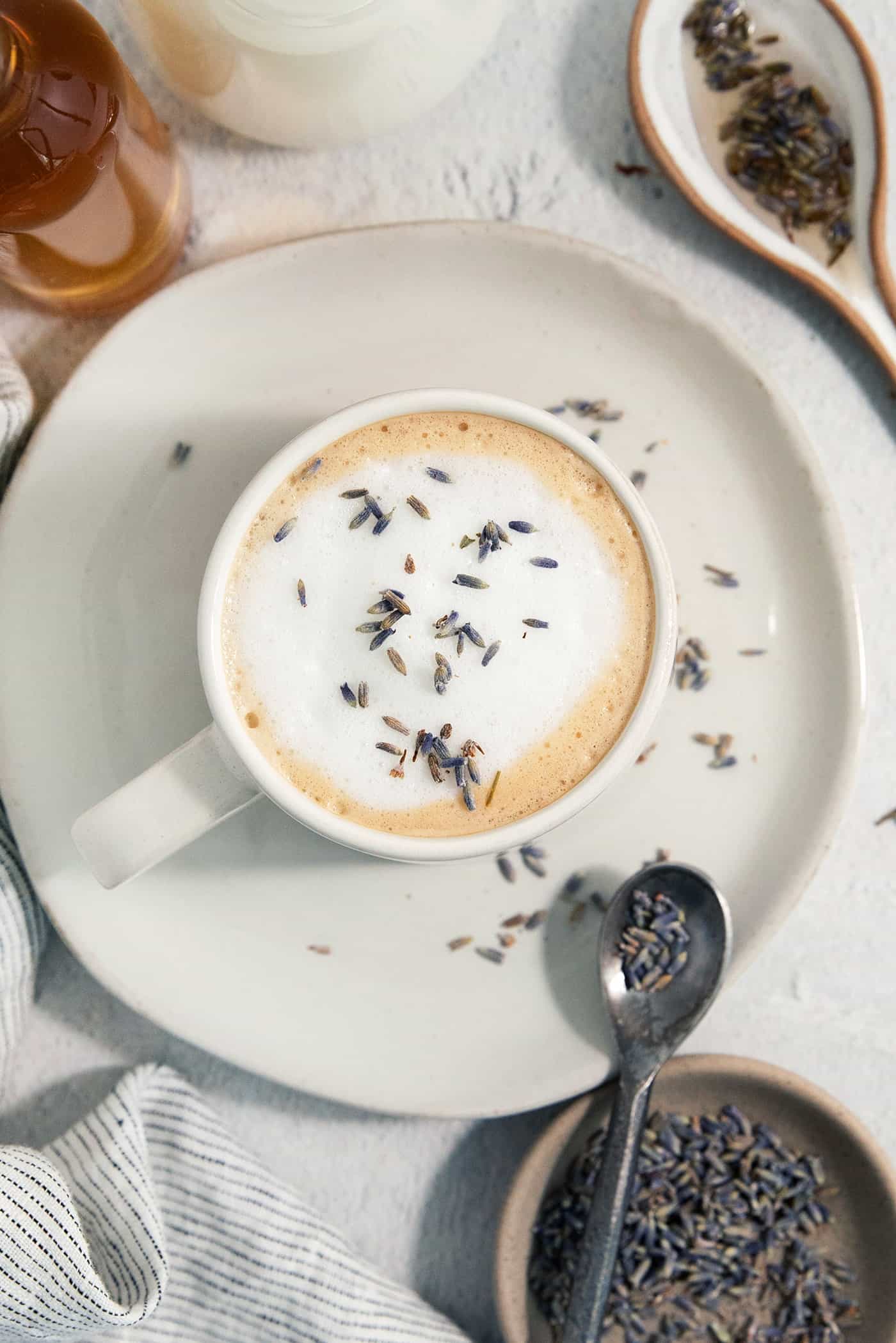 This Lavender Latte mixes freshly brewed espresso, oat milk, and a sweet lavender simple syrup to create a copycat Starbucks lavender latte. Lavender tops a creamy lavender latte on a plate.