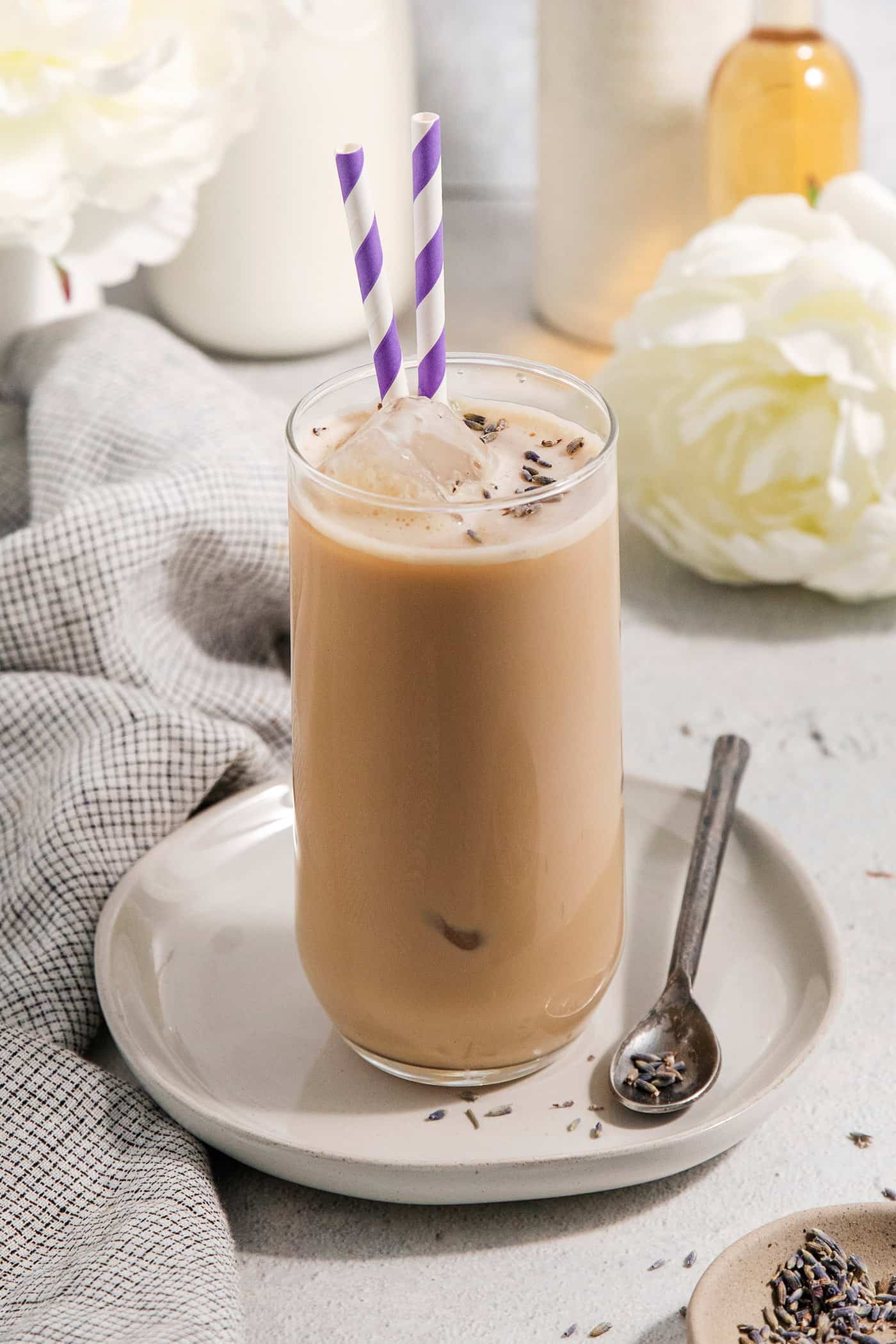 This Lavender Latte mixes freshly brewed espresso, oat milk, and a sweet lavender simple syrup to create a copycat Starbucks lavender latte. A glass of lavender latte on a plate with a spoon.