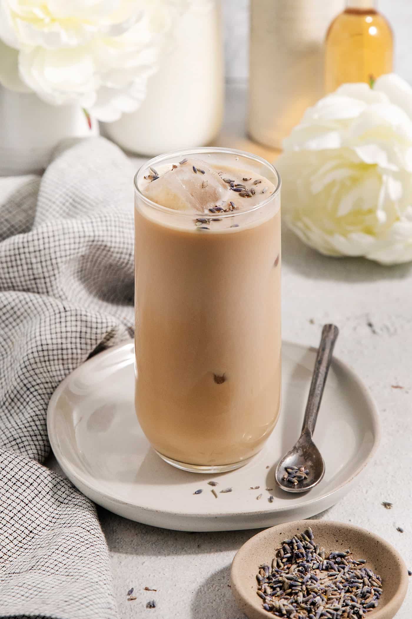 Floral lavender infuses this Lavender Simple Syrup with a hint of sweetness and fresh flavor. Swirl it into coffee and add it to cocktails. A little dish of lavender is shown next to a plate that holds a glass of lavender latte.
