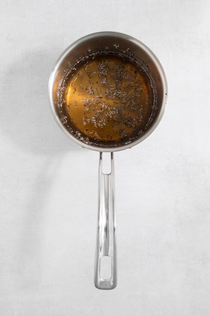Floral lavender infuses this Lavender Simple Syrup with a hint of sweetness and fresh flavor. Swirl it into coffee and add it to cocktails. A saucepan holds the ingredients for lavender simple syrup as they cook.