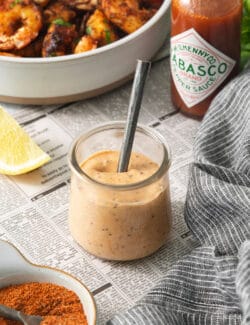 A jar of shrimp dipping sauce with a spoon in it shown in front of a bowl of blackened shrimp.