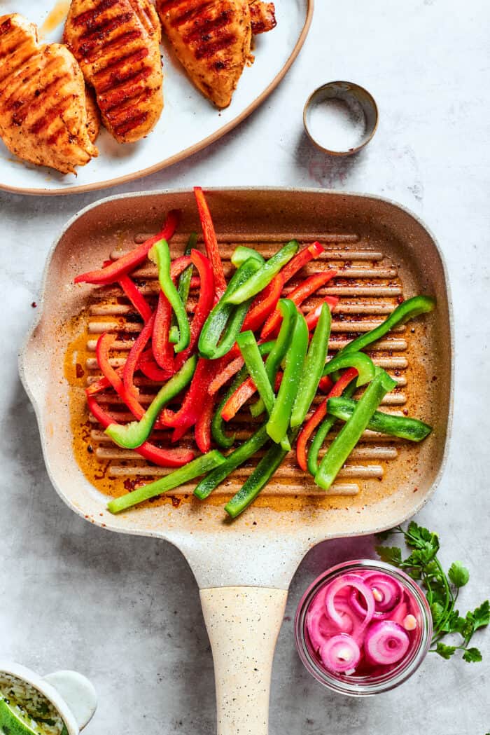 Juicy Honey Mustard Chicken Kabobs are slicked in a smoky honey mustard sauce and cooked to perfection on the grill. Red and green bell pepper slices cook on a grill.
