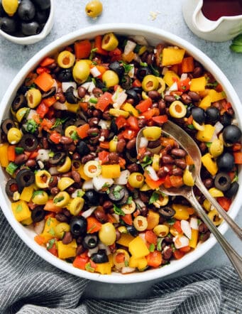 Serving utensils rest in a big bowl of black bean salsa.