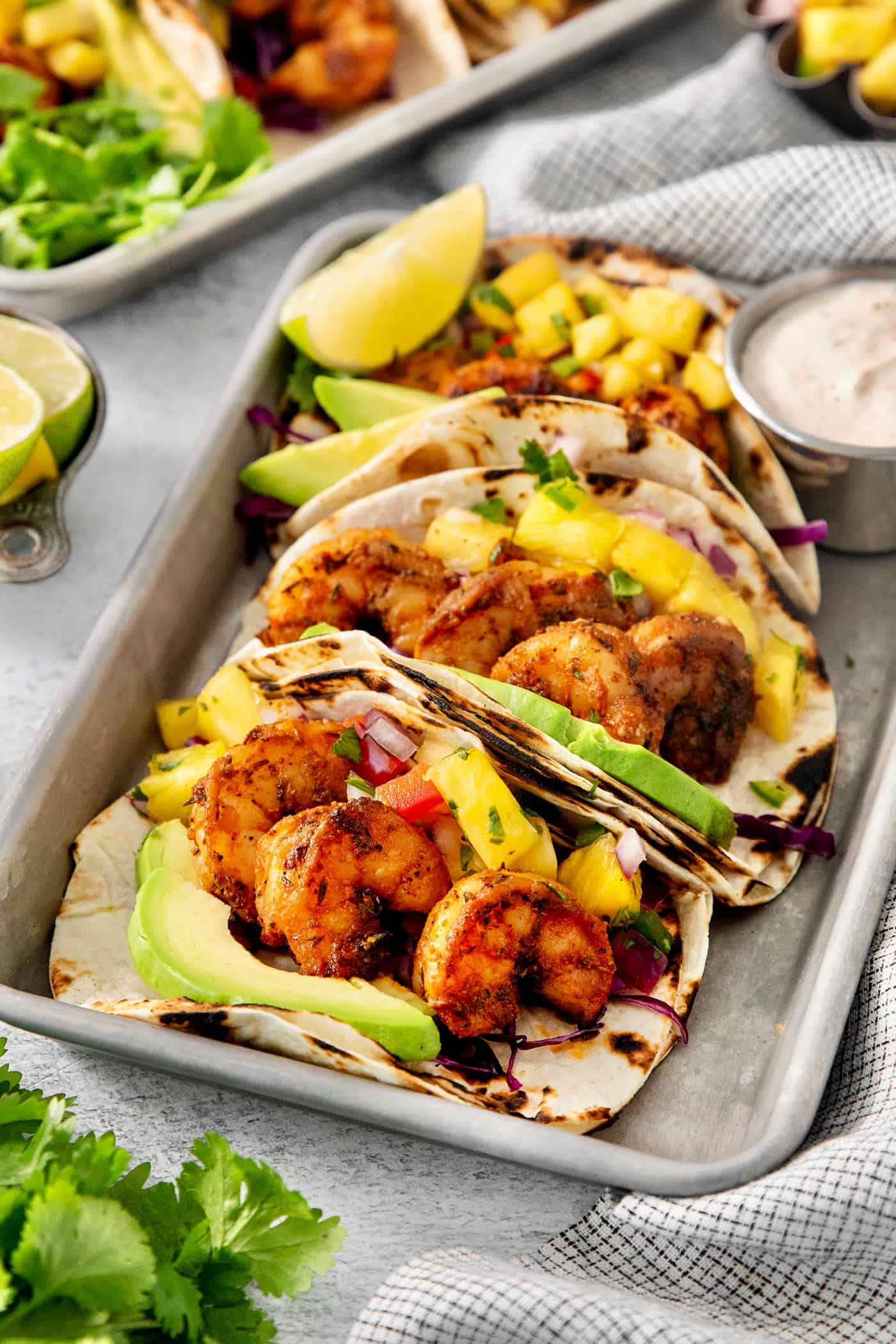 These blackened shrimp tacos feature charred flour tortillas stuffed with spicy blackened shrimp, pineapple salsa, and refreshing lime crema. Trays of blackened shrimp tacos with lime wedges and avocado crema.