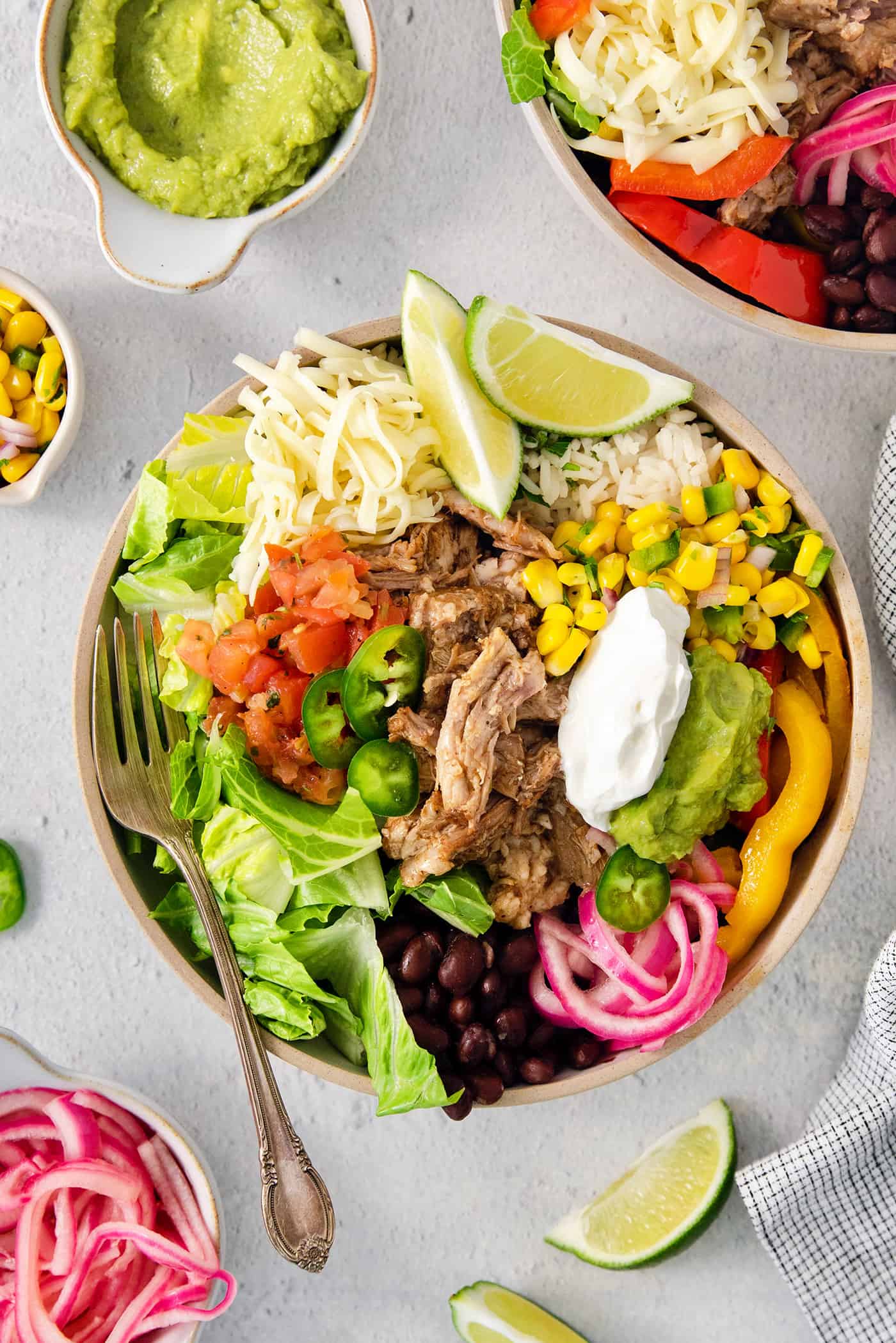 These Carnitas Burrito Bowls layer carnitas, black beans, citrusy cilantro lime rice, and pico de gallo for a better-than-takeout meal. A colorful carnitas burrito bowl surrounded by toppings.