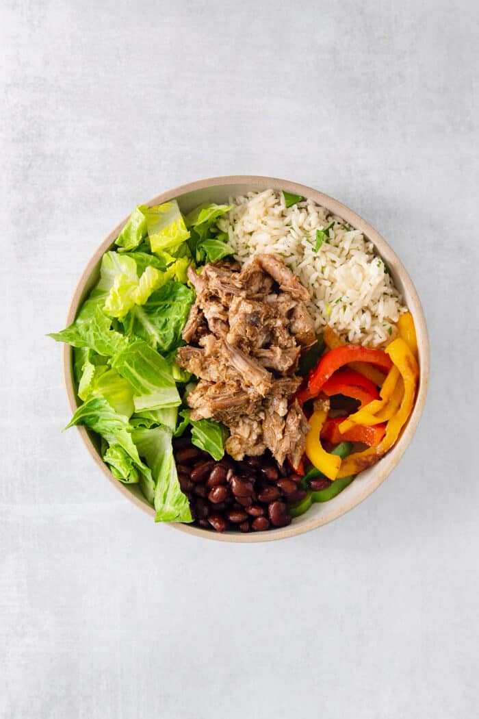These Carnitas Burrito Bowls layer carnitas, black beans, citrusy cilantro lime rice, and pico de gallo for a better-than-takeout meal. The ingredients are layered into a bowl for carnitas bowls.