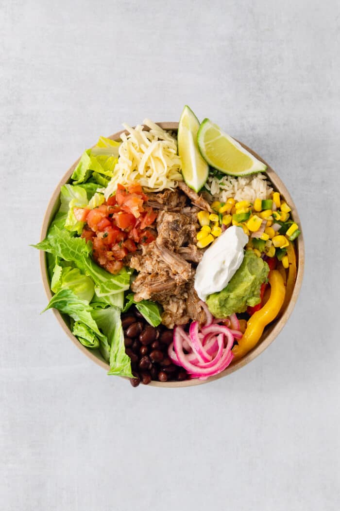 These Carnitas Burrito Bowls layer carnitas, black beans, citrusy cilantro lime rice, and pico de gallo for a better-than-takeout meal. The salsas, guacamole, and sour cream are added to the top of the carnitas burrito bowl.