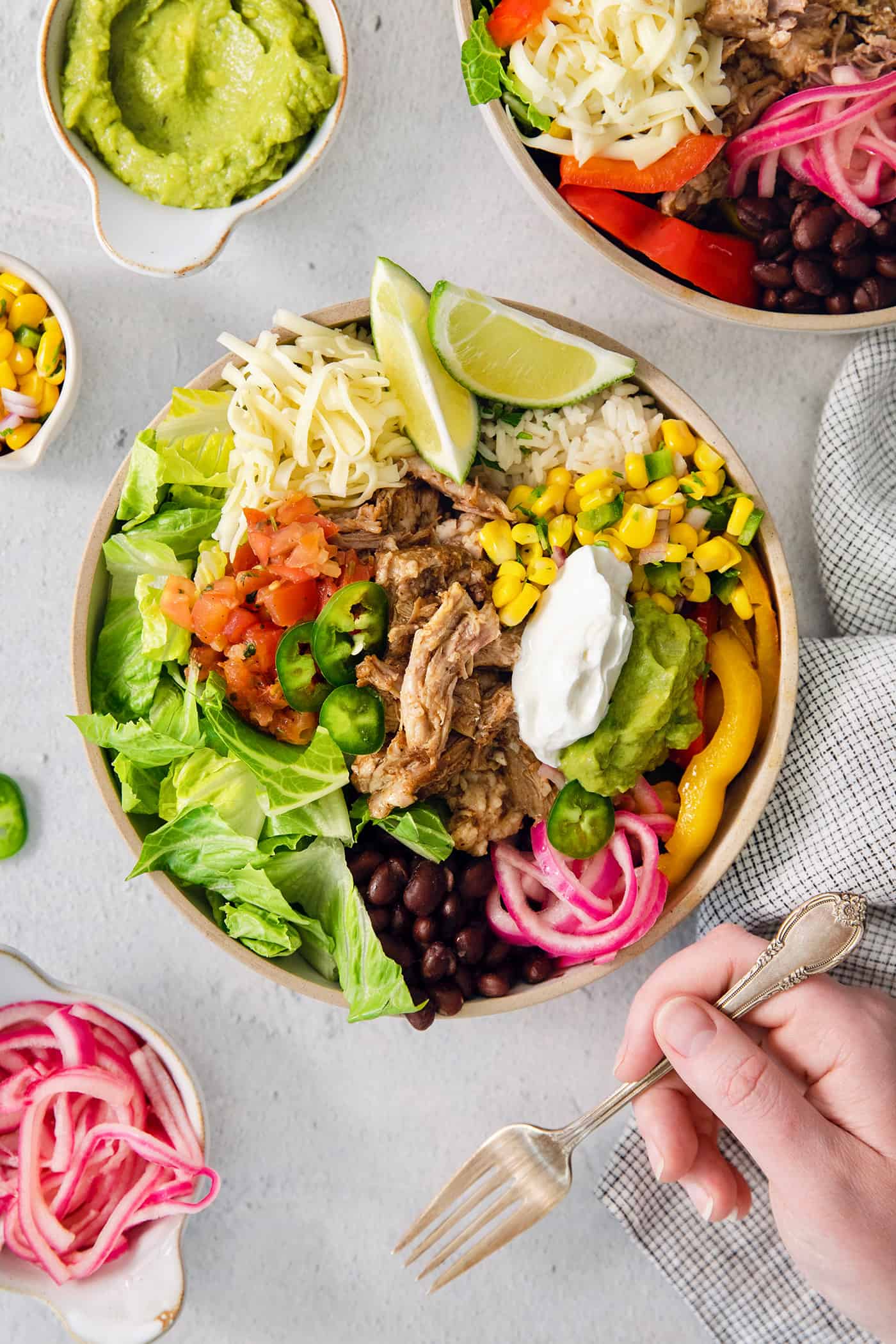 These Carnitas Burrito Bowls layer carnitas, black beans, citrusy cilantro lime rice, and pico de gallo for a better-than-takeout meal. A carnitas burrito bowl topped with lime guacamole, and sour cream is ready to eat.