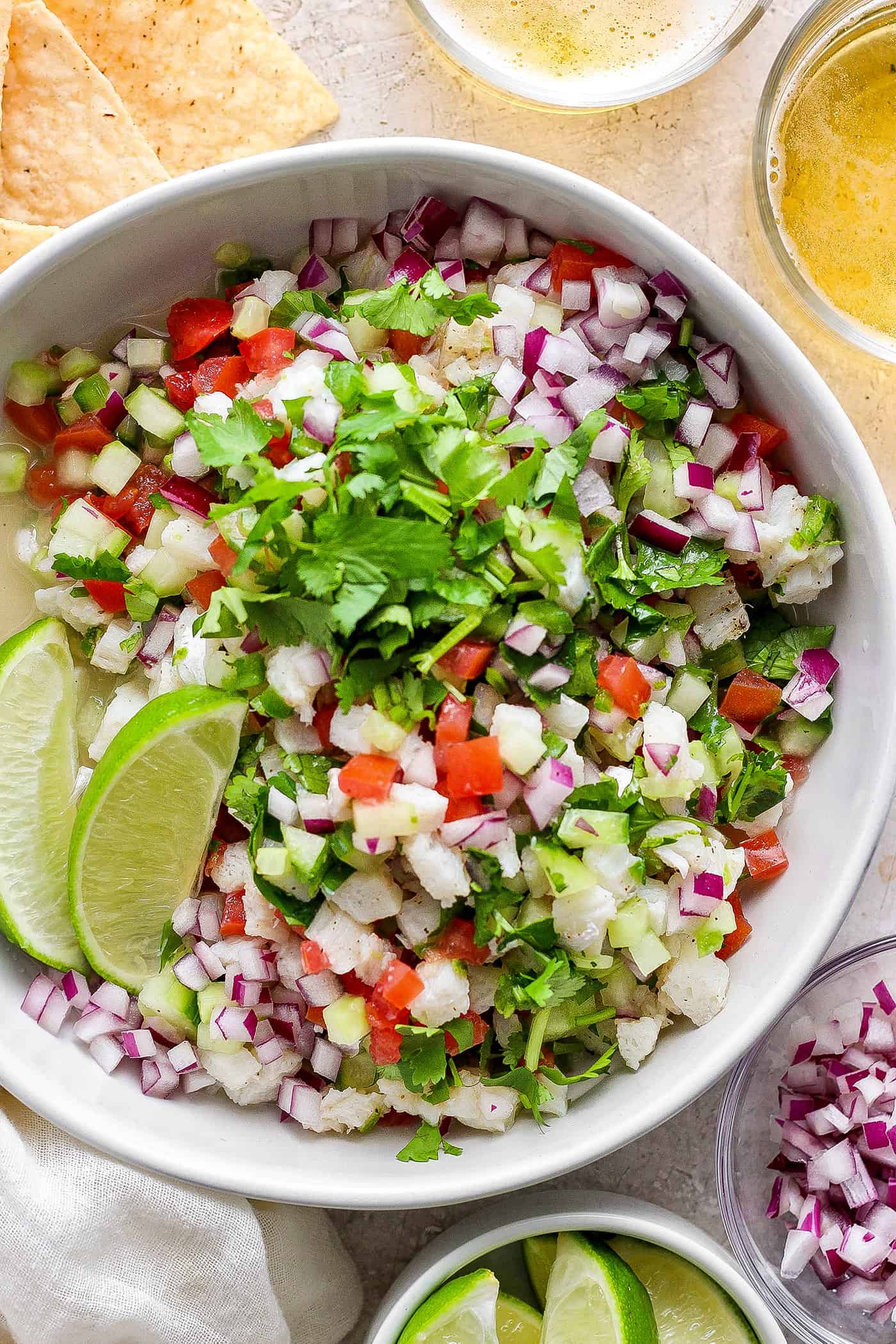 This refreshing Classic Ceviche recipe marinates fresh fish in lime and orange juices, then adds a mix of fresh veggies and a bit of jalapeno. A bowl of classic ceviche with lime wedges.