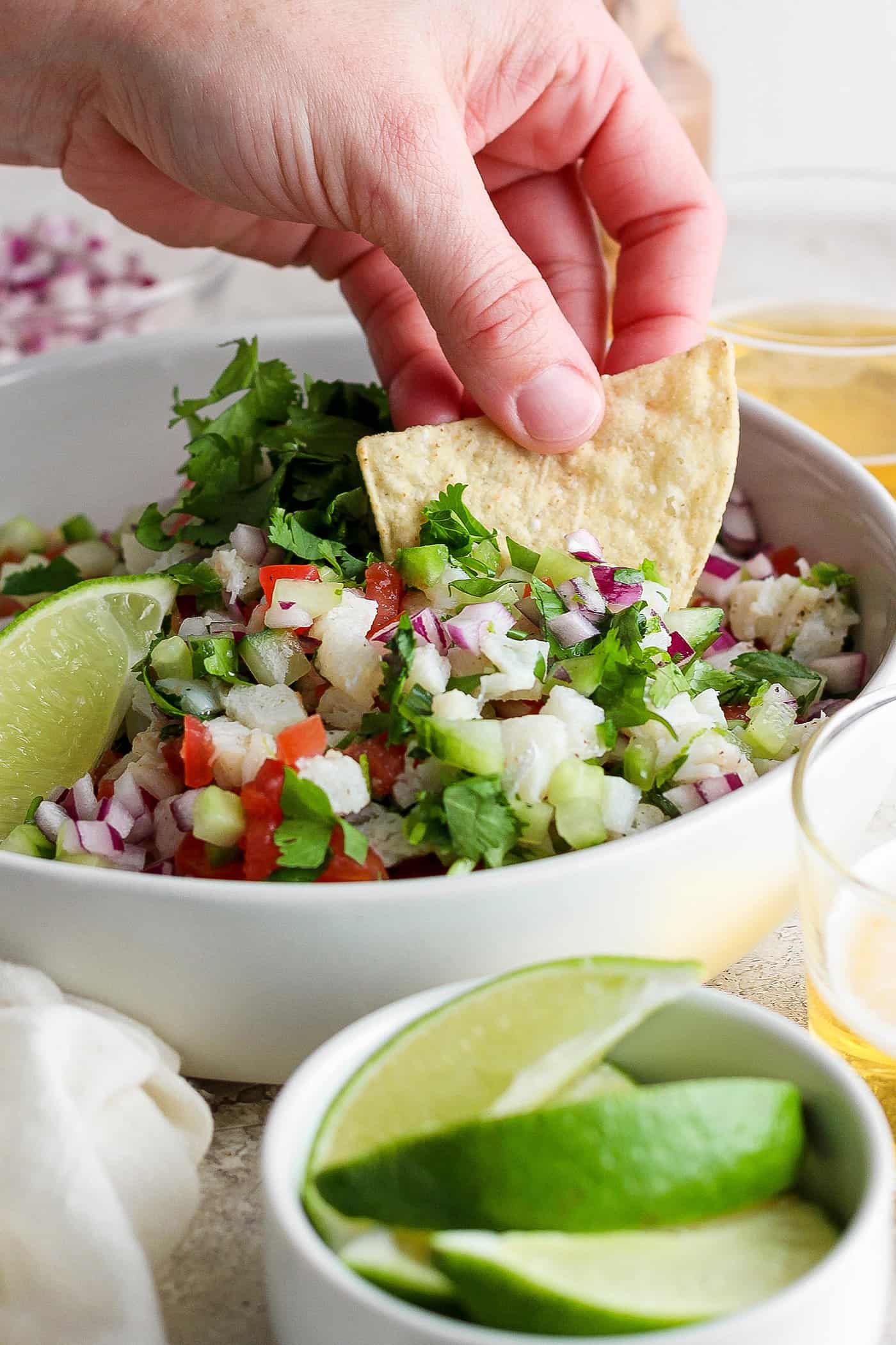 This refreshing Classic Ceviche recipe marinates fresh fish in lime and orange juices, then adds a mix of fresh veggies and a bit of jalapeno. A hand dips a tortilla chip into a bowl of classic ceviche.