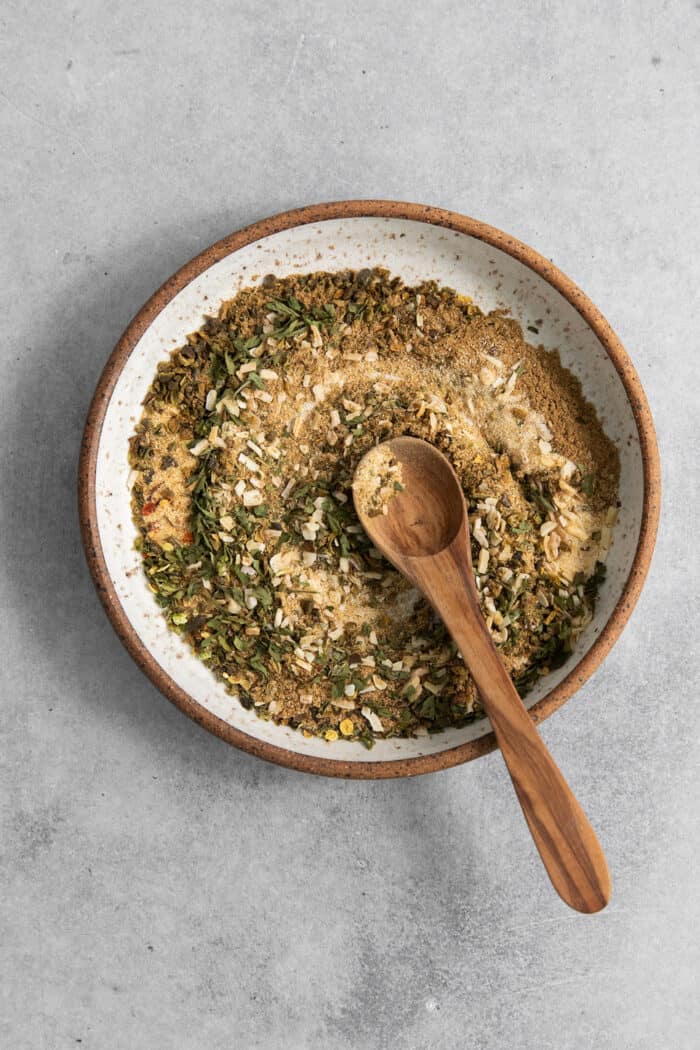 Homemade Green Taco Seasoning is so easy to DIY! It's flavorful, not too spicy, and is perfect in tacos, nachos, quesadillas and more. A wooden spoon stirs a bowl of spices for green taco seasoning.