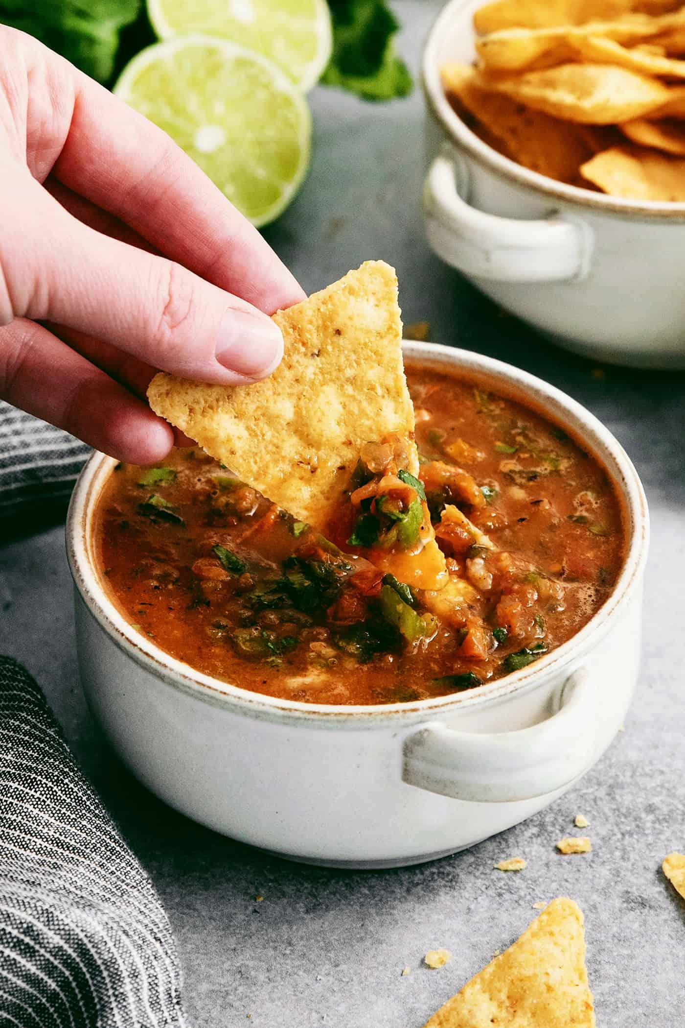 This Warm Salsa recipe is perfectly spiced and juicy, with a pop of lime juice for sweetness. Enjoy it with tacos, quesadillas, & chips. A hand dips a tortilla chip into a bowl of warm salsa.