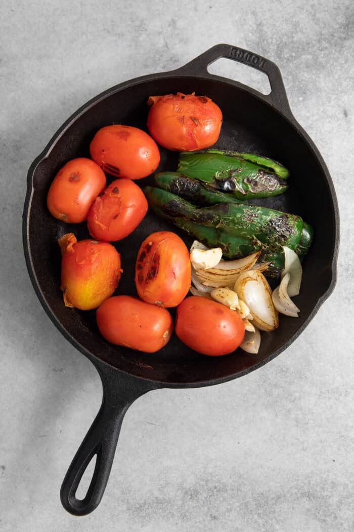 This Warm Salsa recipe is perfectly spiced and juicy, with a pop of lime juice for sweetness. Enjoy it with tacos, quesadillas, & chips. A cast iron skillet holds tomatoes, garlic, and green peppers.