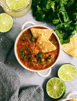 A white bowl of warm salsa topped with tortilla chips.