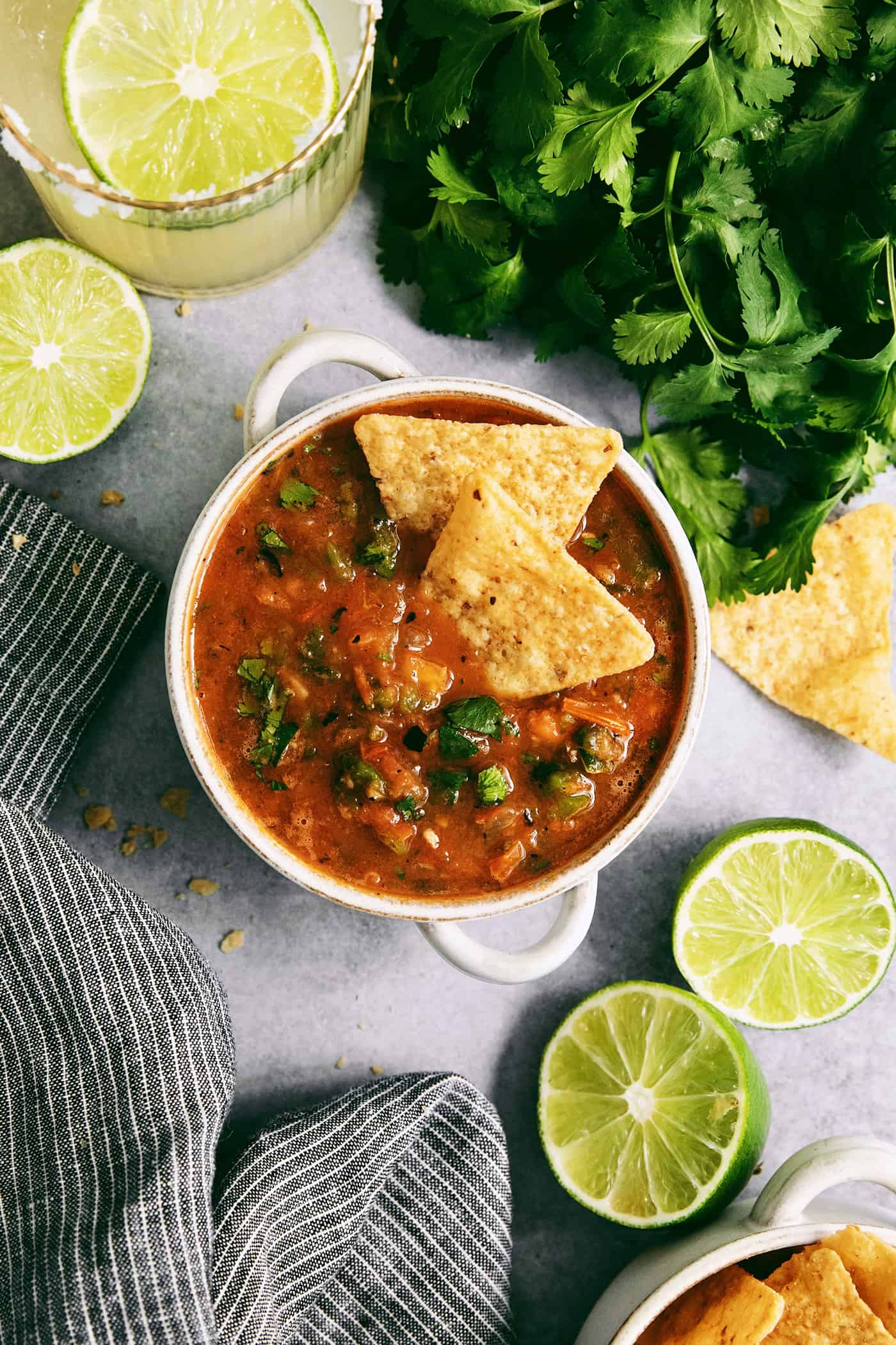 This Warm Salsa recipe is perfectly spiced and juicy, with a pop of lime juice for sweetness. Enjoy it with tacos, quesadillas, & chips. A white bowl of warm salsa topped with tortilla chips.