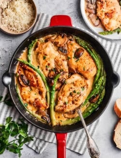overhead photo of chicken breasts, asparagus, and mushrooms in a skillet, with Madeira sauce