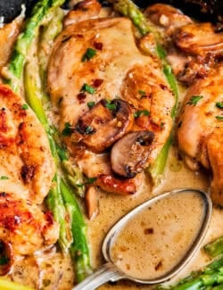 chicken breasts and asparagus in a skillet, with a spoon full of Madeira sauce