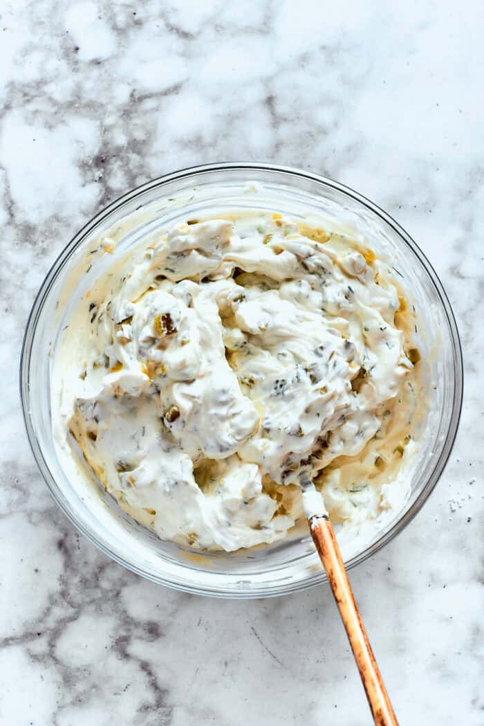 This cold and creamy Dill Pickle Dip is packed with crunchy pickles and a mix of cream cheese and sour cream. A spoon folds dill pickle dip.