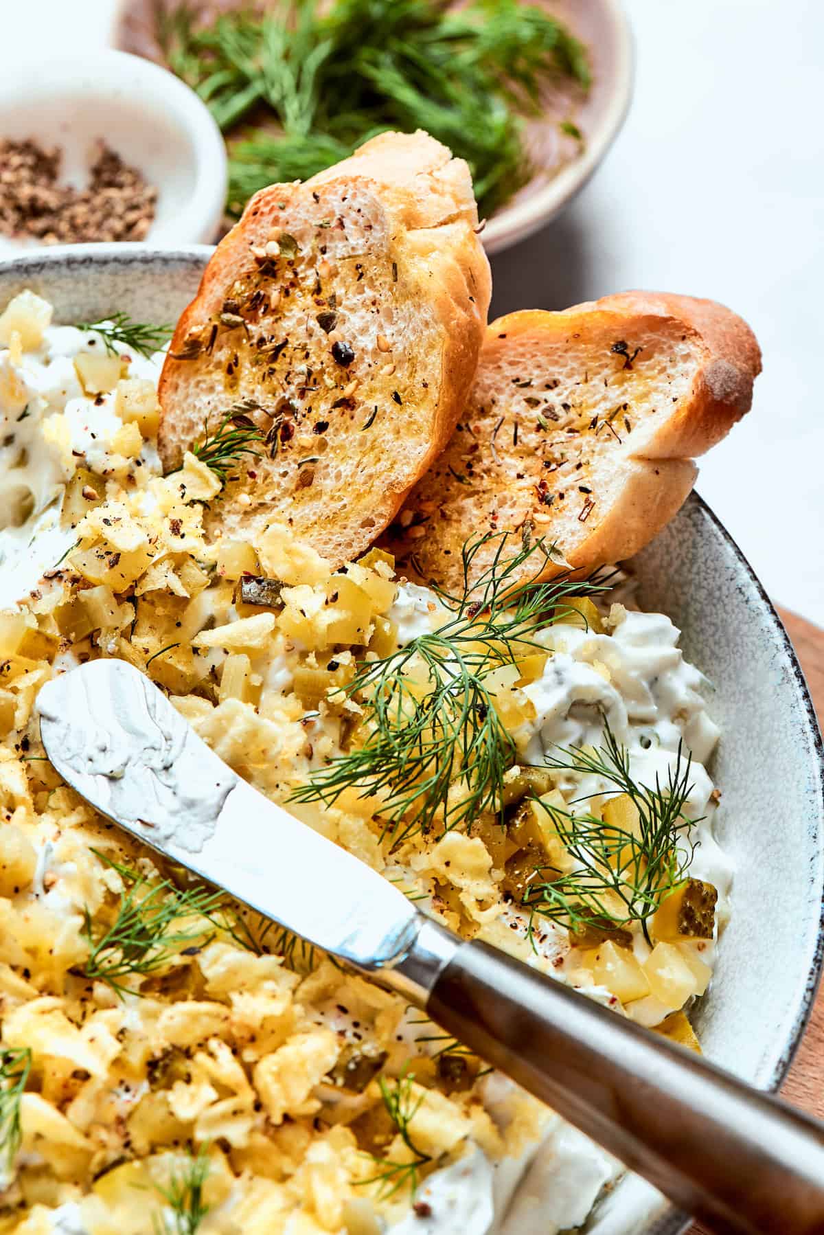 This cold and creamy Dill Pickle Dip is packed with crunchy pickles and a mix of cream cheese and sour cream. A knife rests on top of a bowl of pickle dip.