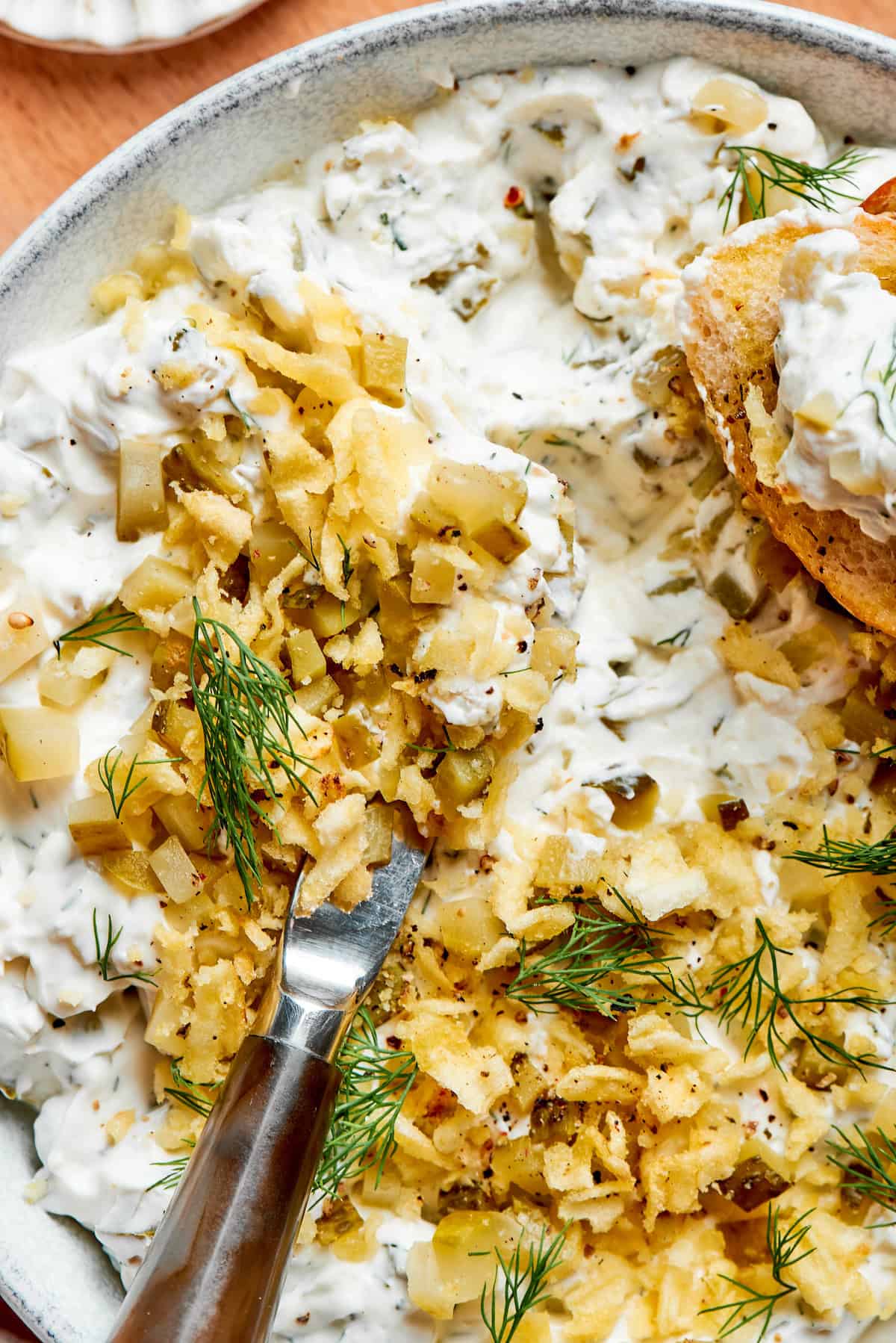 This cold and creamy Dill Pickle Dip is packed with crunchy pickles and a mix of cream cheese and sour cream. A knife digs into a bowl of dill pickle dip.