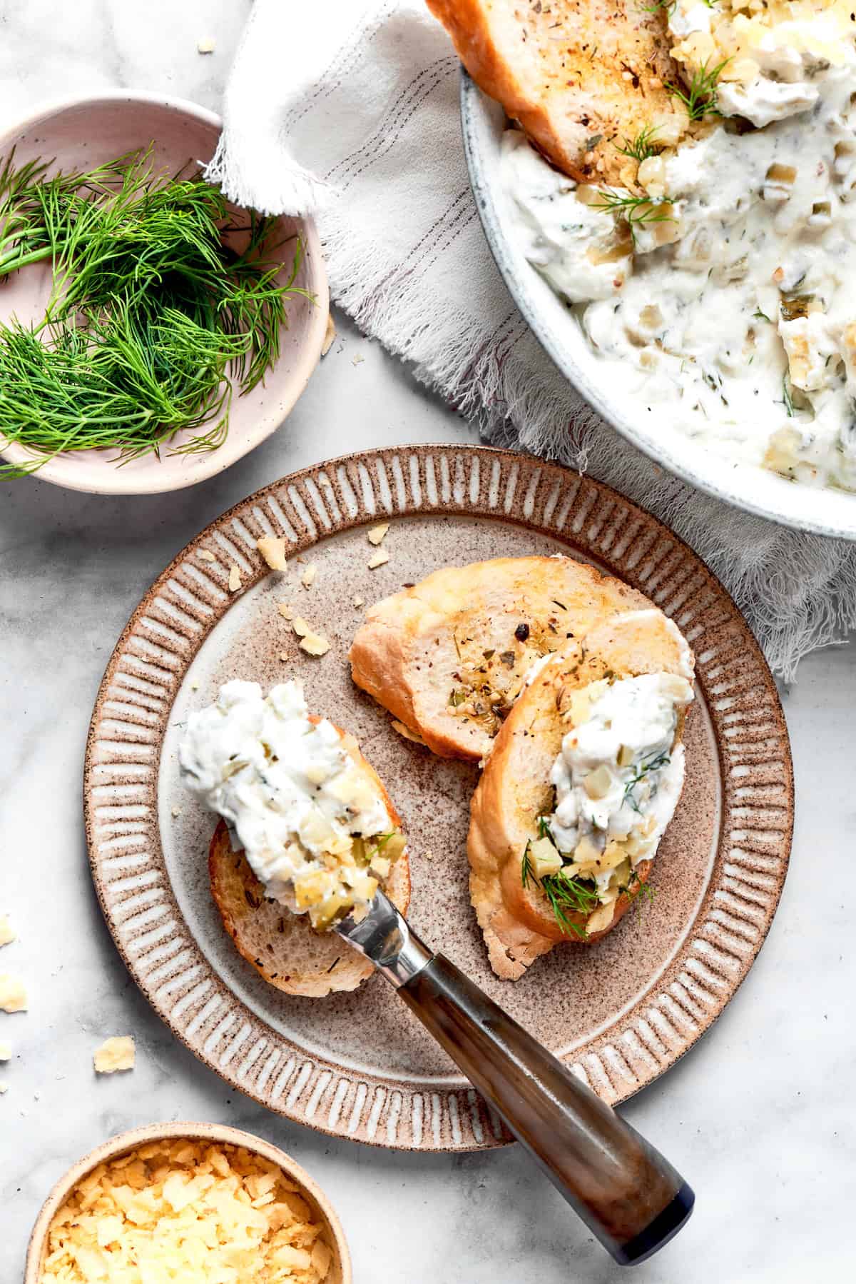 This cold and creamy Dill Pickle Dip is packed with crunchy pickles and a mix of cream cheese and sour cream. Dill pickle dip is spread on a slice of baguette with a knife.