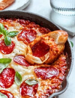 A cheesy pan of baked pizza dip and a slice of bread.
