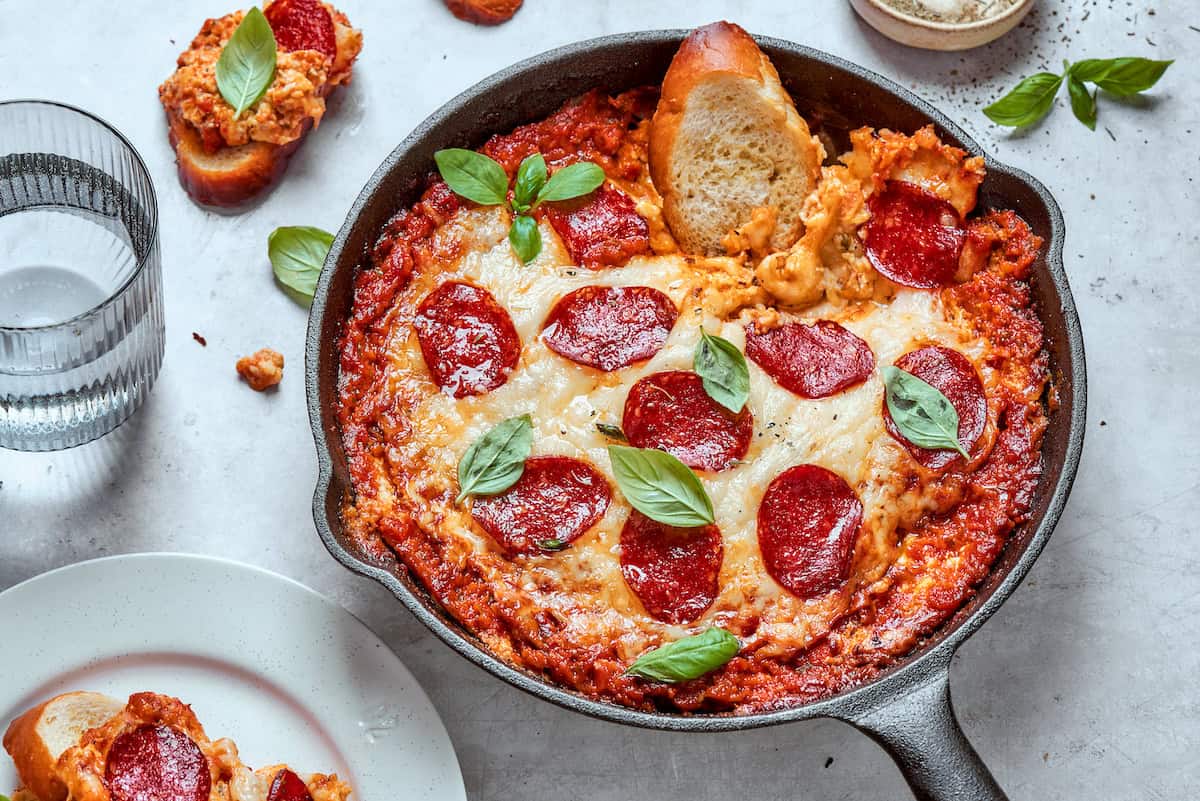 A slice of bread is dipped into a pan of pizza dip.